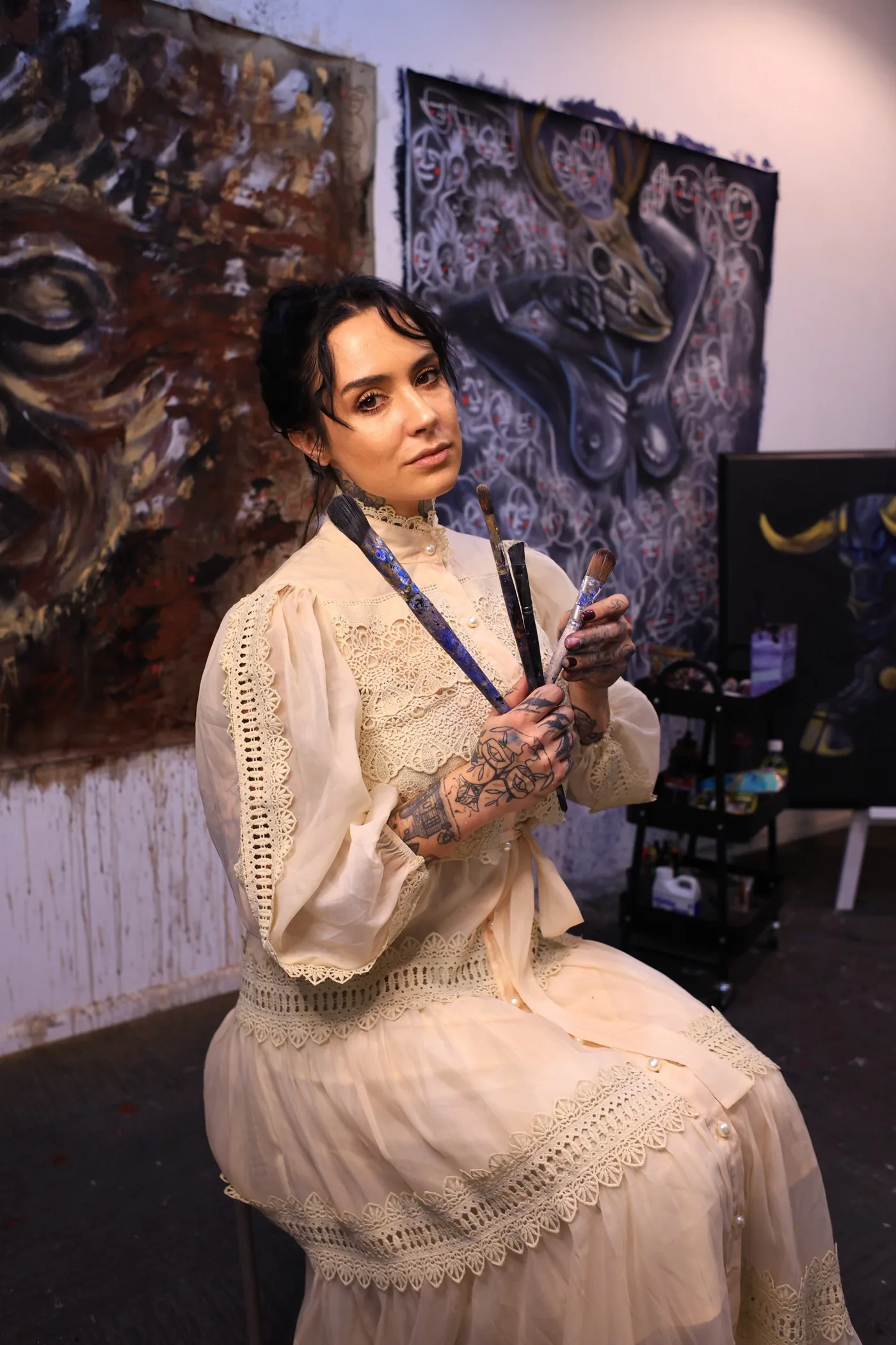 The artist in the studio, brushes in hand, in front of her paintings